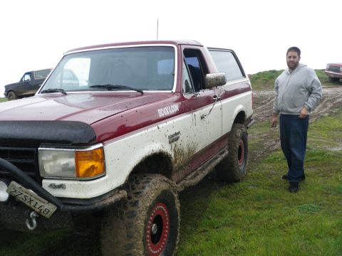 1991 Ford Bronco - A two-tone red and white Ford Bronco is parked on a muddy field with a man standing nearby.