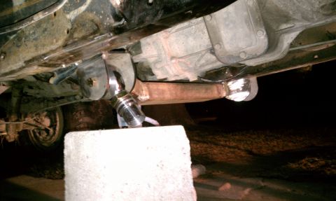 1990 Ford Bronco - Modified suspension parts visible on the underside of a vehicle, supported by a concrete block.
