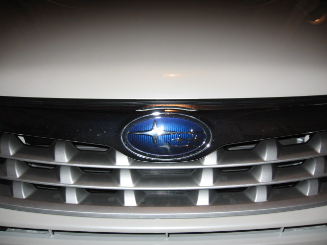 Blue and chrome Subaru badge on the silver grille of a white vehicle, close-up at night