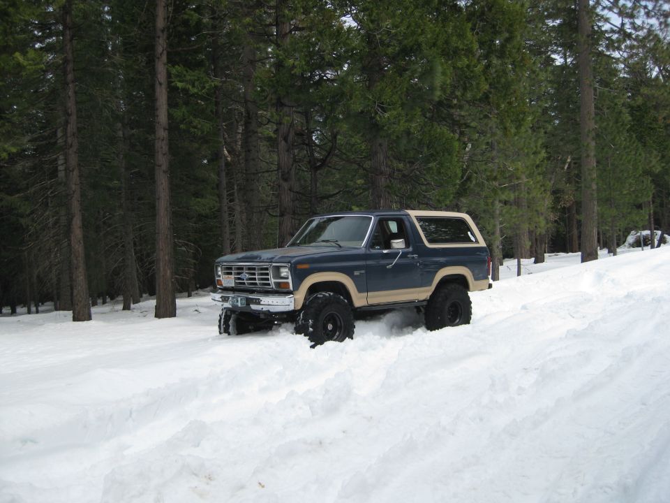 Blue and tan 1986 Ford Bronco driving in deep snow