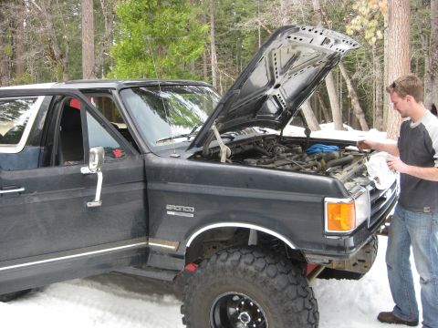 1986 Ford Bronco - Man works on the engine of a 1986 Ford Bronco parked in a snowy, wooded area.