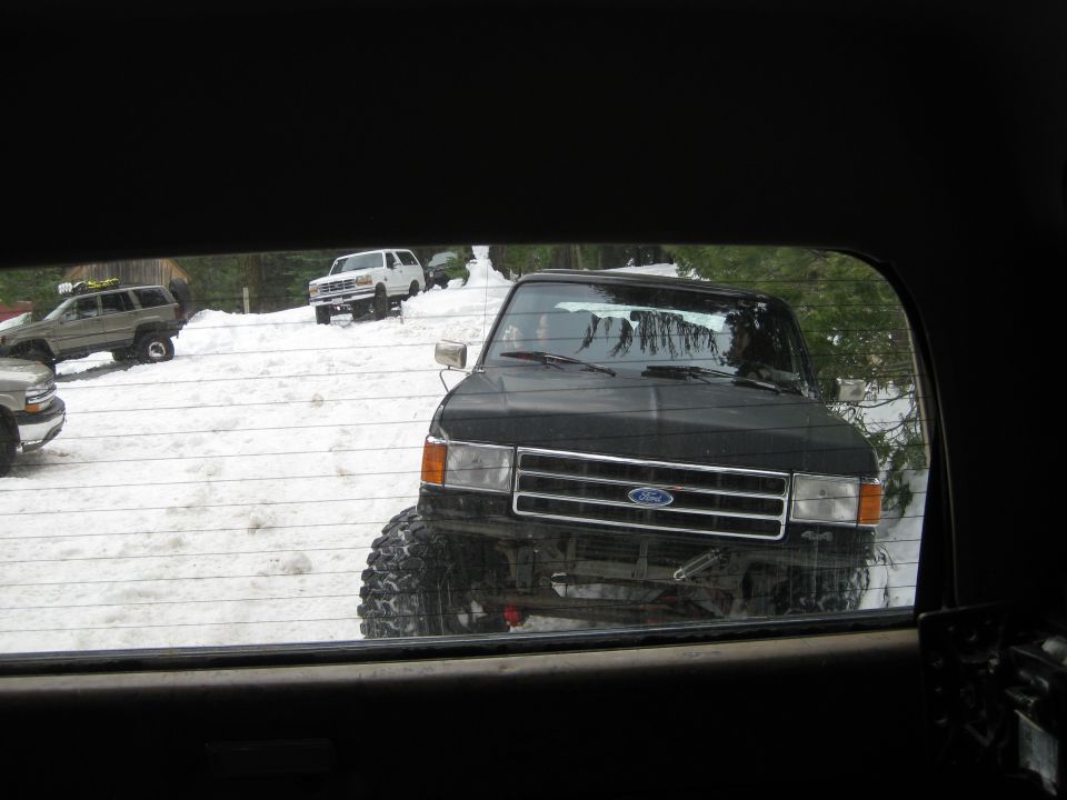 black lifted pickup truck with large tires in snow, other SUVs and trucks visible in background