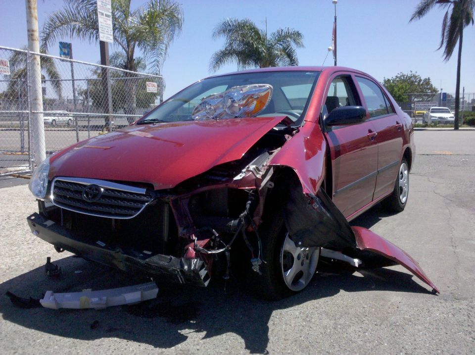 Maroon Toyota sedan with heavy front-end crash damage in a paved lot