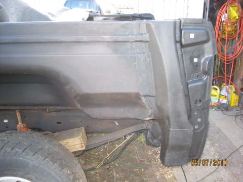 1983 Ford Bronco - Close-up view of the rear quarter panel and tailgate support structure of a vehicle, showing suspension components and wiring.