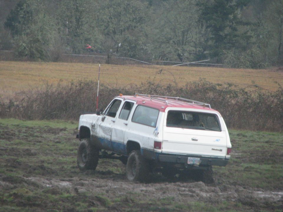 White and red SUV with lifted suspension driving through mud. License plate is visible