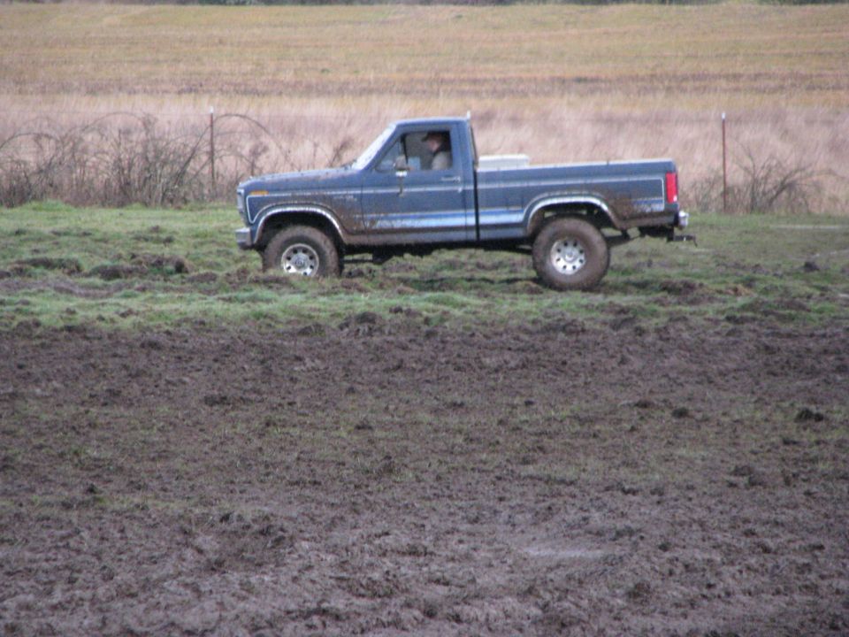 Blue pickup truck driving through a muddy field. It looks like a 1979 Ford F-Series