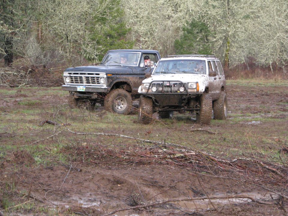 Black Ford F-Series truck and white Jeep Cherokee in mud. Truck has a 1975 grille