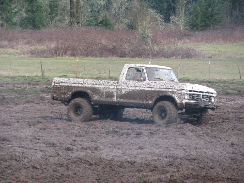 Muddy pickup truck driving through a muddy field. Looks like a 1975 Ford F-Series