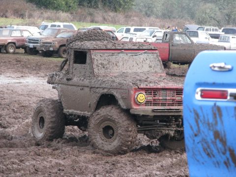1978 Ford Bronco - A heavily mud-caked 1978 Ford Bronco navigates a muddy terrain, with other vehicles visible in the background.