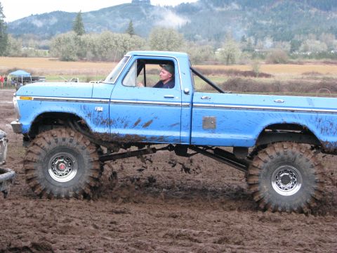 1978 Ford Bronco - A blue pickup truck navigates a muddy terrain with its large tires.