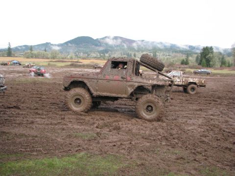 1978 Ford Bronco - A heavily mud-covered vehicle navigates a challenging off-road course with other vehicles in the background.