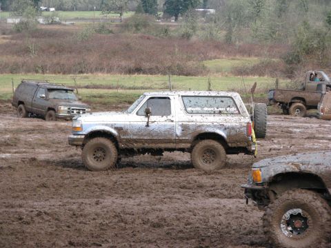 1978 Ford Bronco - Several vehicles are stuck in a muddy field, including a white SUV with "SuperMotors.net" visible on its rear window.