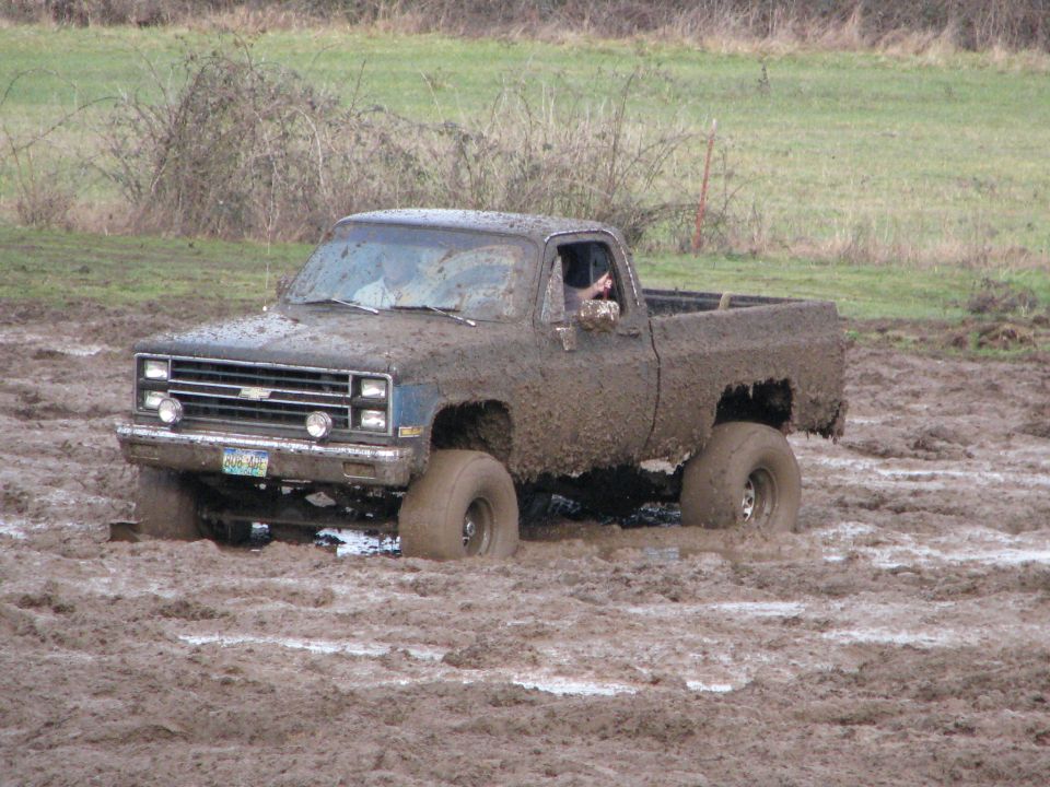 Mud-covered pickup truck stuck in mud, front grille visible