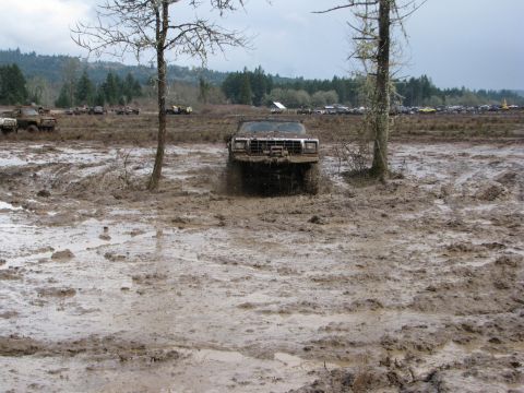 1978 Ford Bronco - An off-road vehicle navigates a challenging muddy terrain with trees and other vehicles in the background.