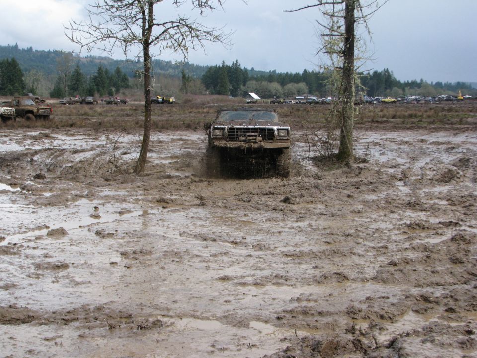 Mud-splattered off-road vehicle with winch, driving through a muddy field