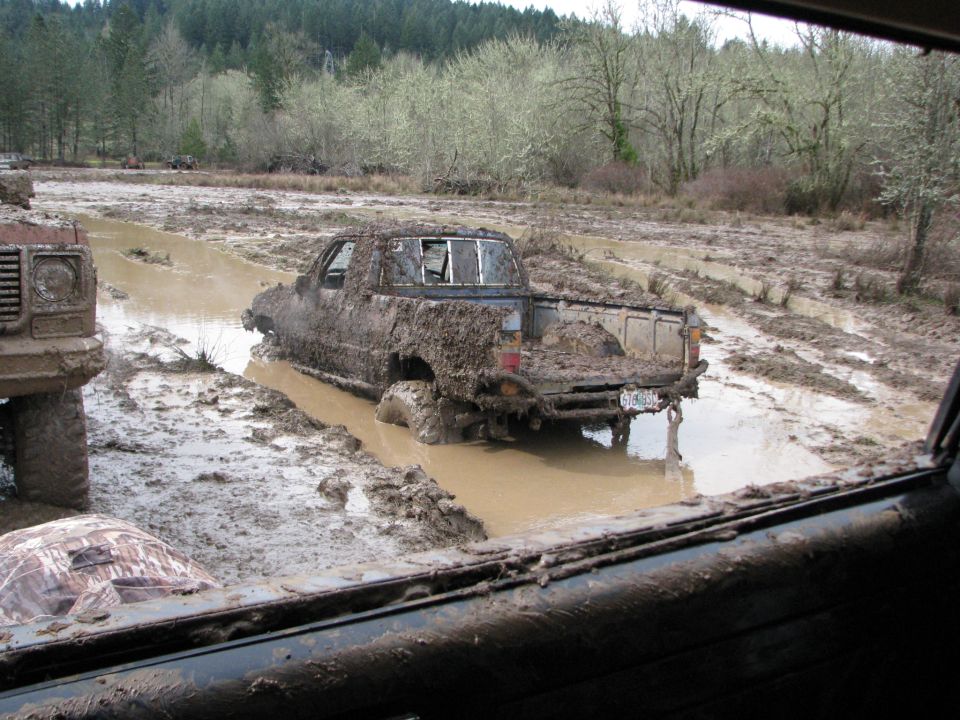 Muddy pickup truck stuck in a mud pit, another vehicle partially visible to the left