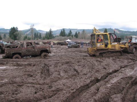 1978 Ford Bronco - A muddy off-road event with multiple vehicles stuck in the mud, a bulldozer attempts to pull one out.