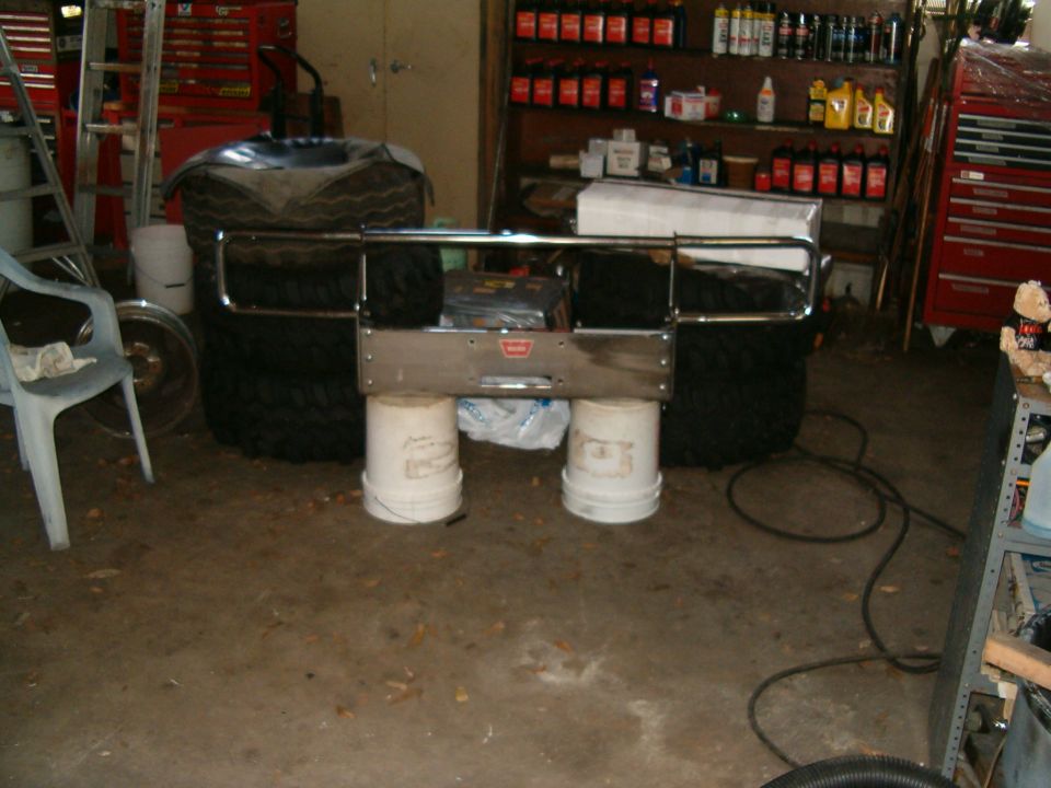 Chrome winch bumper with brush guard and Warn winch plate staged on buckets in a garage