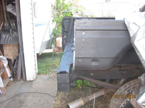 1983 Ford Bronco - This photo shows the rear body panel of a vehicle, partially covered by a tarp, with a trailer and propane tank visible.
