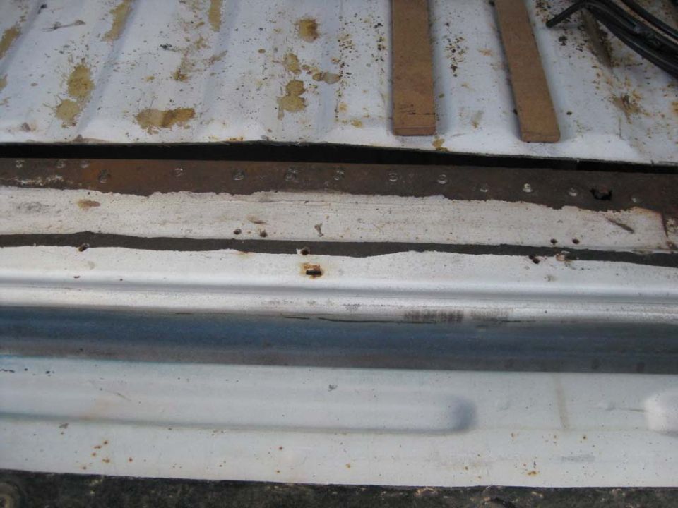 Rusty tub support rail and spot welds under a white Bronco floor pan