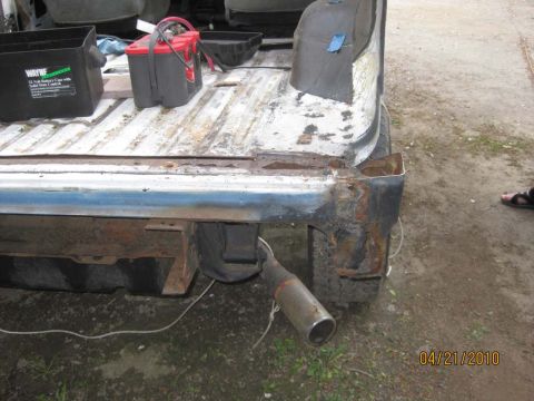 1983 Ford Bronco - Rear three-quarter view of a stripped white body tub with the quarter panel cut away to expose a badly rusted rear corner and inner structu…