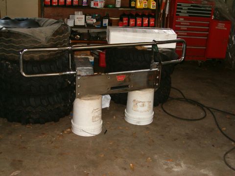 1991 Ford Bronco - A winch bumper with a WARN logo is shown, supported by buckets and resting on tires.