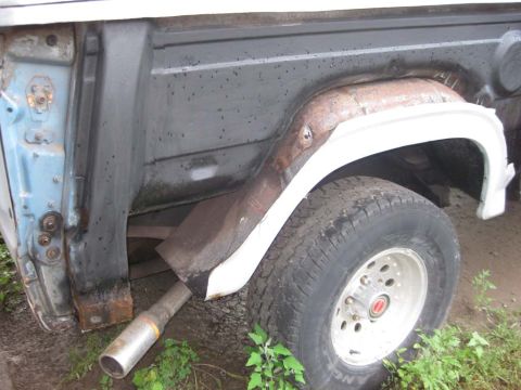 1983 Ford Bronco - Close view down the passenger-side rear quarter of a Bronco with the outer skin removed, exposing the gray inner tub wall, the rusty wheel-…
