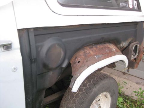 1983 Ford Bronco - Passenger-side rear of a Bronco with the outer quarter skin cut away, revealing the gray inner tub, the heavily surface-rusted inner wheelh…