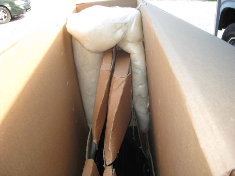 1983 Ford Bronco - White foam padding or headliner material packed inside a large cardboard box sitting in the bed of a truck, with a car and a spare tire vis…