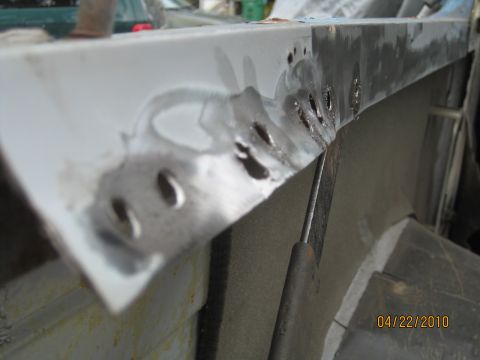 1983 Ford Bronco - Tight macro along the upper flange of a white-painted quarter panel showing a row of drilled-out spot welds and ground-down metal where the…