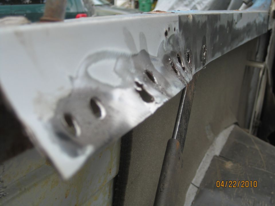 Row of drilled-out spot welds along a white quarter panel flange during removal