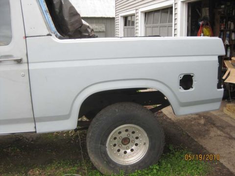 1983 Ford Bronco - Side view of a topless Bronco with a freshly fitted rear quarter panel in gray primer, showing the open taillight cutout, empty wheel arch…