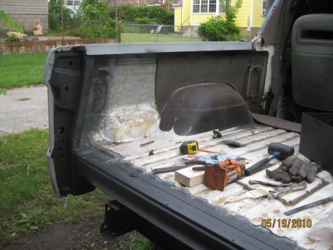 1983 Ford Bronco - Rear cargo area of a stripped Bronco tub with the tailgate down, showing bare and stained sheet metal, a primered inner quarter with old cr…