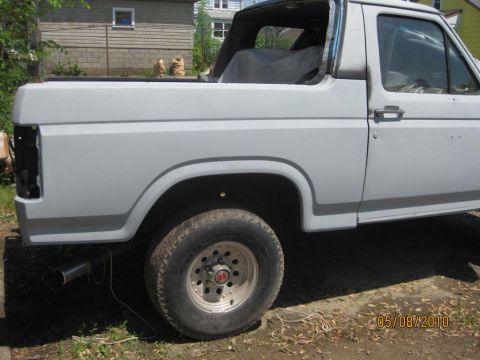 1983 Ford Bronco - Driver's-side rear three-quarter view of a topless full-size Bronco in uniform gray primer, with the replacement quarter panel hung and the…