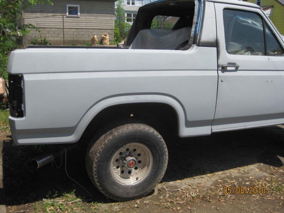 Topless Ford Bronco in gray primer, driver-side rear quarter with empty taillight opening