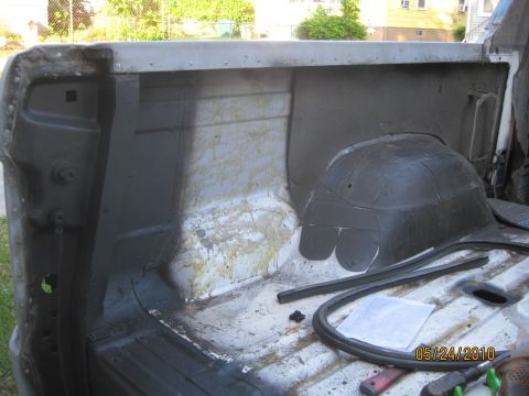 1983 Ford Bronco - Looking down into the stripped rear cargo tub of an open-top Bronco, with bare and primered inner quarter panels, a patch of old peeling cr…