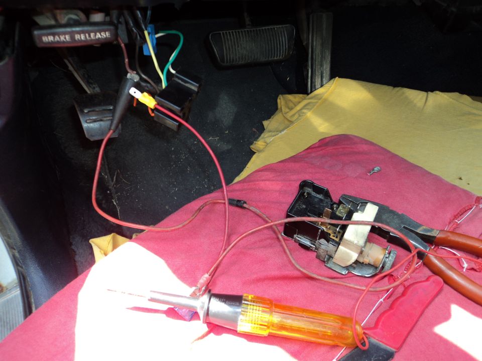 Interior view of car floor with brake release lever, wiring, and electrical testing tools