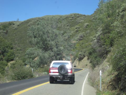 1989 Ford Bronco - A white Ford Bronco is seen from behind driving on a two-lane road with yellow dividing lines.