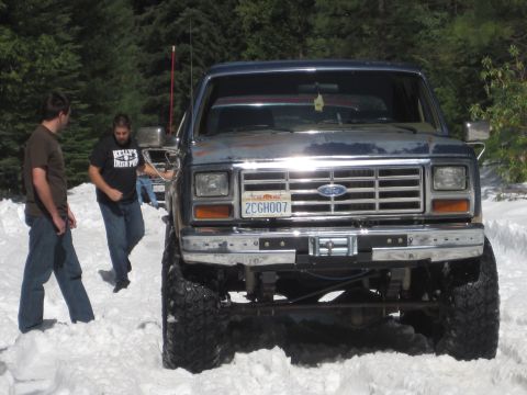 1989 Ford Bronco - Lifted 1980s Ford Bronco with off-road tires parked in a snowy wooded area.