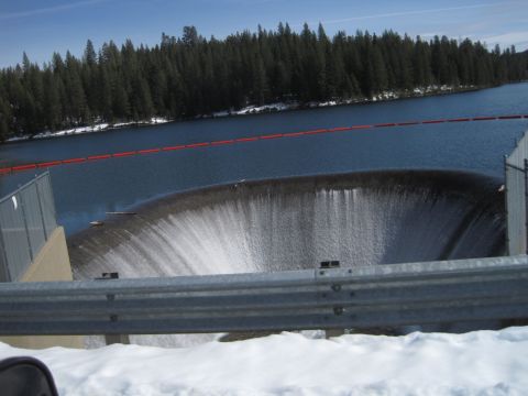 1989 Ford Bronco - Water cascades over a spillway, with a dense forest and snow-covered ground visible in the background.