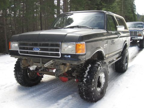 1989 Ford Bronco - Two Ford Broncos parked on a snowy road, one in the foreground is heavily modified.
