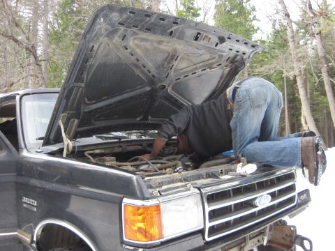 1989 Ford Bronco - A person works on the engine of a truck in a snowy, wooded area.