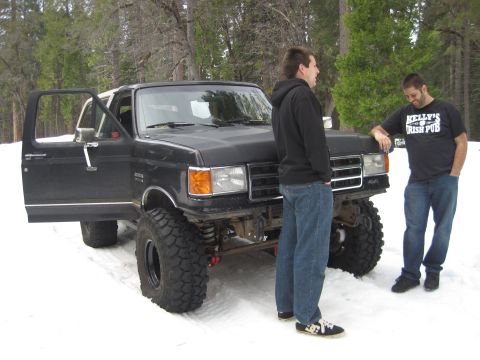 1989 Ford Bronco - A lifted black 1989 Ford Bronco sits in the snow with its driver's door open, two men standing nearby.
