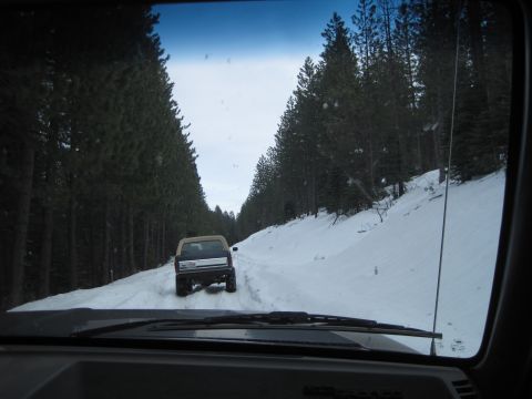 1989 Ford Bronco - Two vehicles navigate a snowy forest road, with one SUV leading the way.