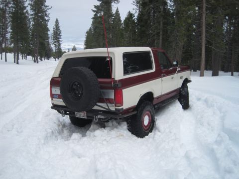 1989 Ford Bronco - A two-tone maroon and white Ford Bronco is stuck in deep snow, with its spare tire visible on the rear.