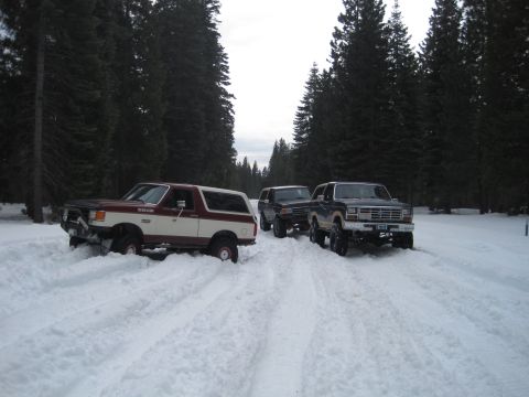 1989 Ford Bronco - Three SUVs navigate a snowy forest road, with a Ford Bronco leading the way.