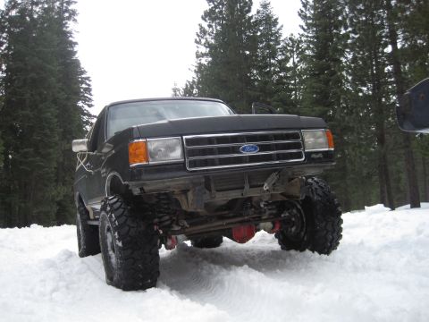 1989 Ford Bronco - A lifted black Ford F-Series truck navigates a snowy terrain.