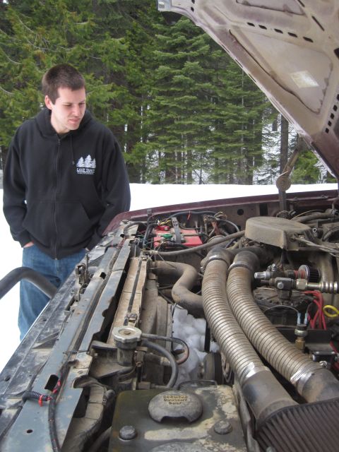 1989 Ford Bronco - A man inspects the engine of a vehicle with its hood open in a snowy, wooded area.