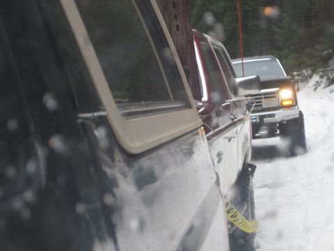 1989 Ford Bronco - Two SUVs drive on a snow-covered road, one behind the other.