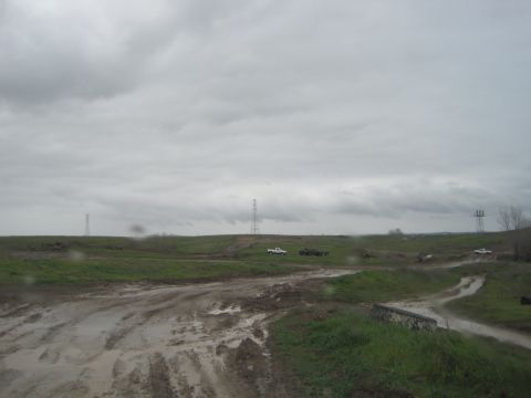 1989 Ford Bronco - Multiple vehicles navigate a challenging muddy terrain with power lines visible in the distance.
